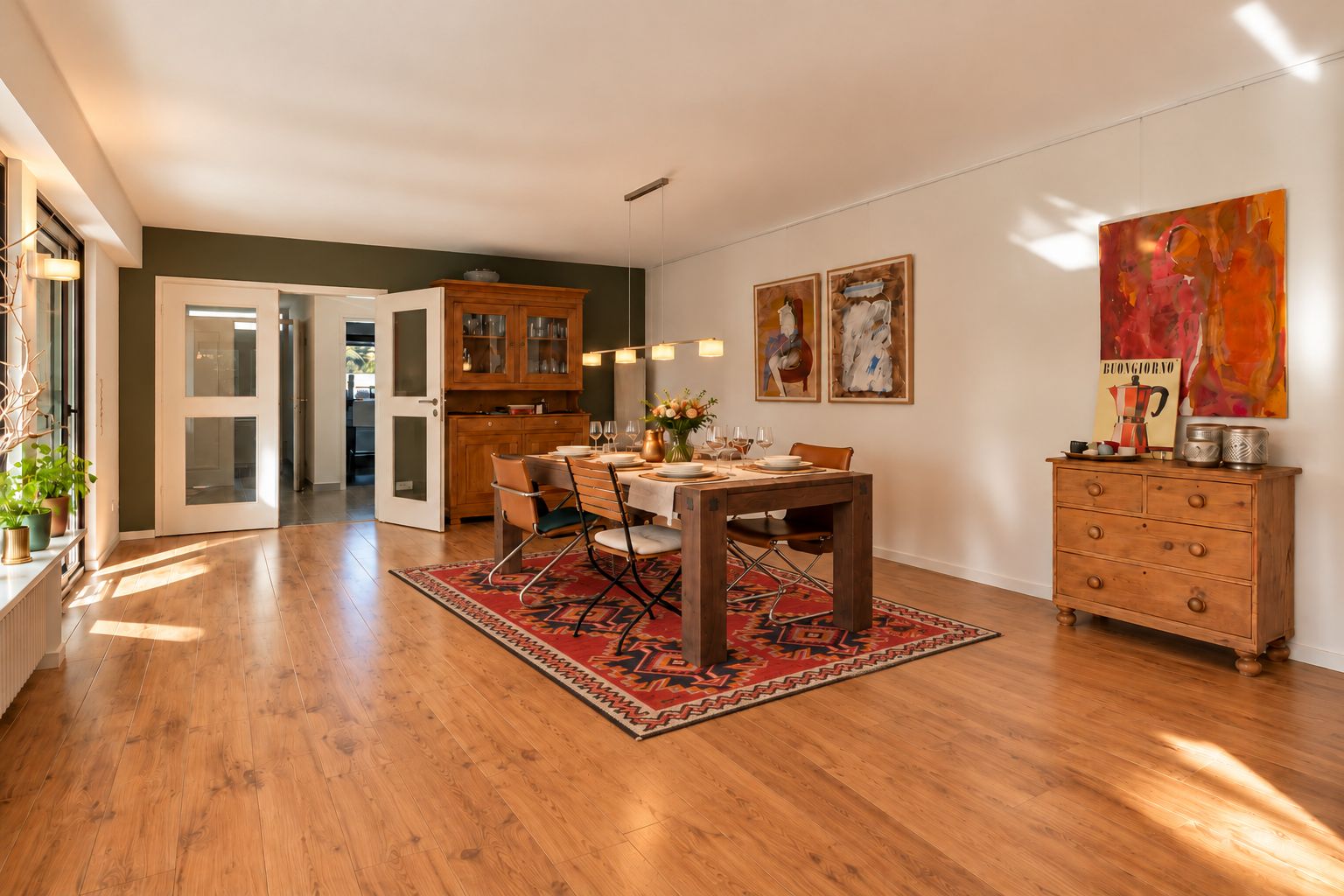 Helles Esszimmer mit Holzboden, Esstisch auf Teppich, Holzmöbeln und Wandbildern.