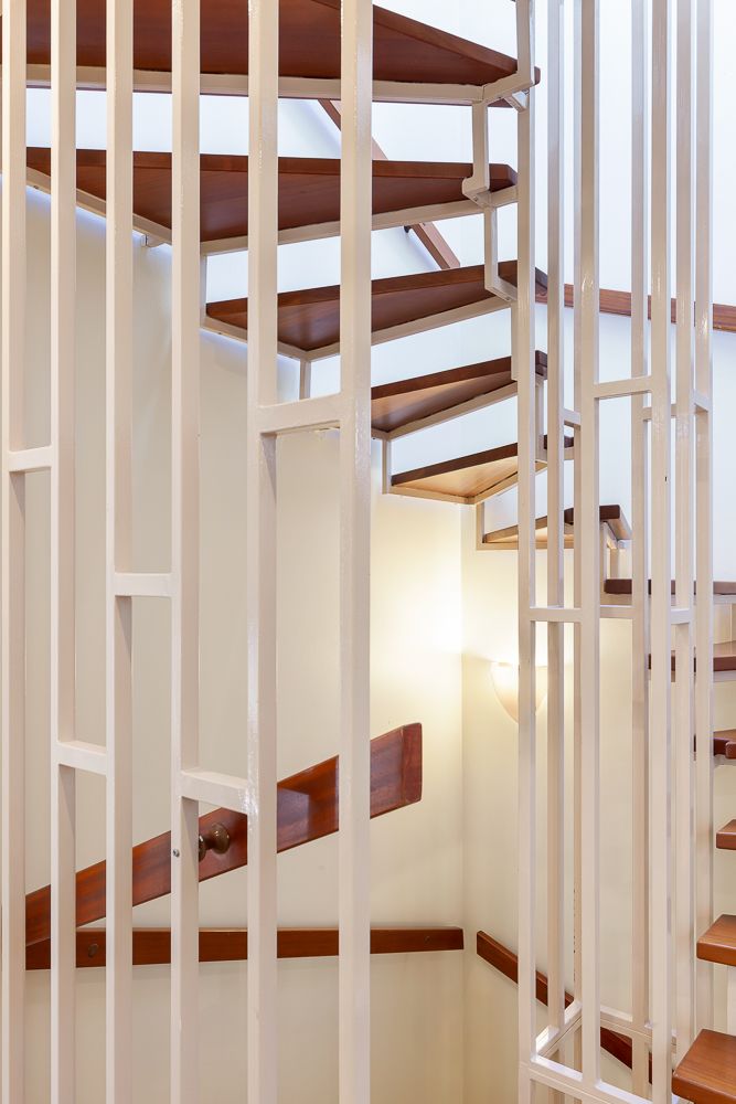 Spiral-Holztreppe mit weißem Metallgeländer in einem Wohnhaus.