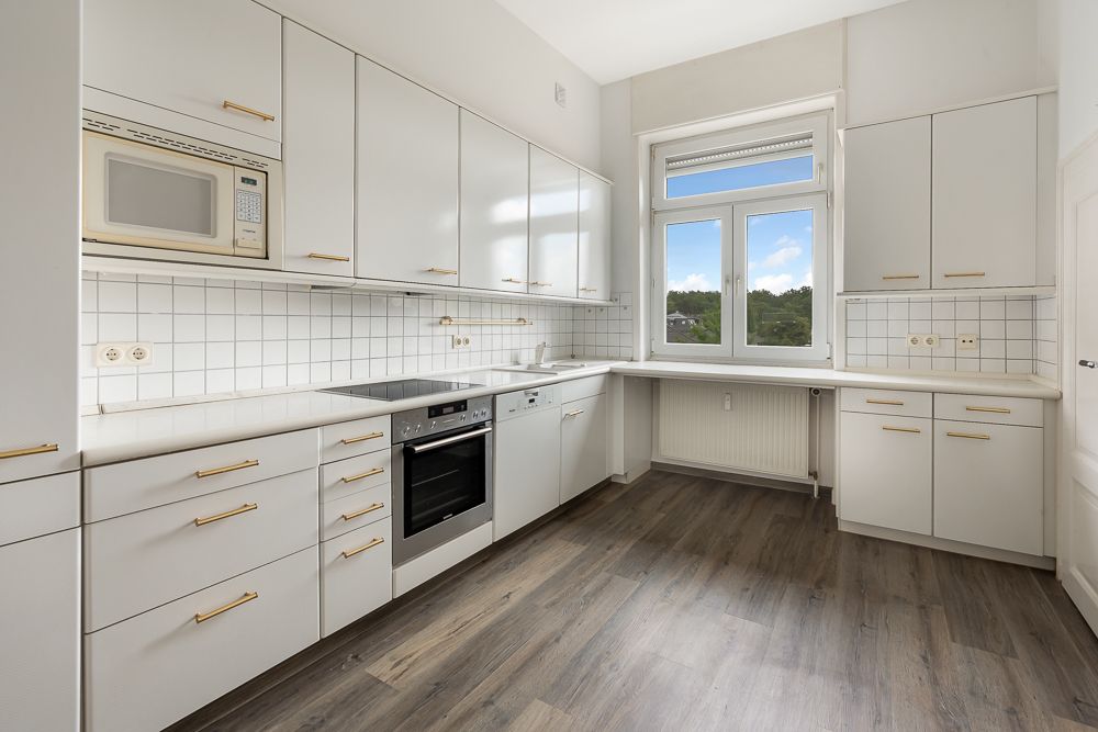 Moderne, helle Küche mit weißen Schränken, Einbaugeräten und großem Fenster.