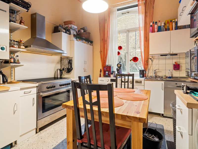 Helle Küche mit Holztisch, vier Stühlen, Herd, Spüle und großem Fenster mit orangefarbenen Vorhängen.
