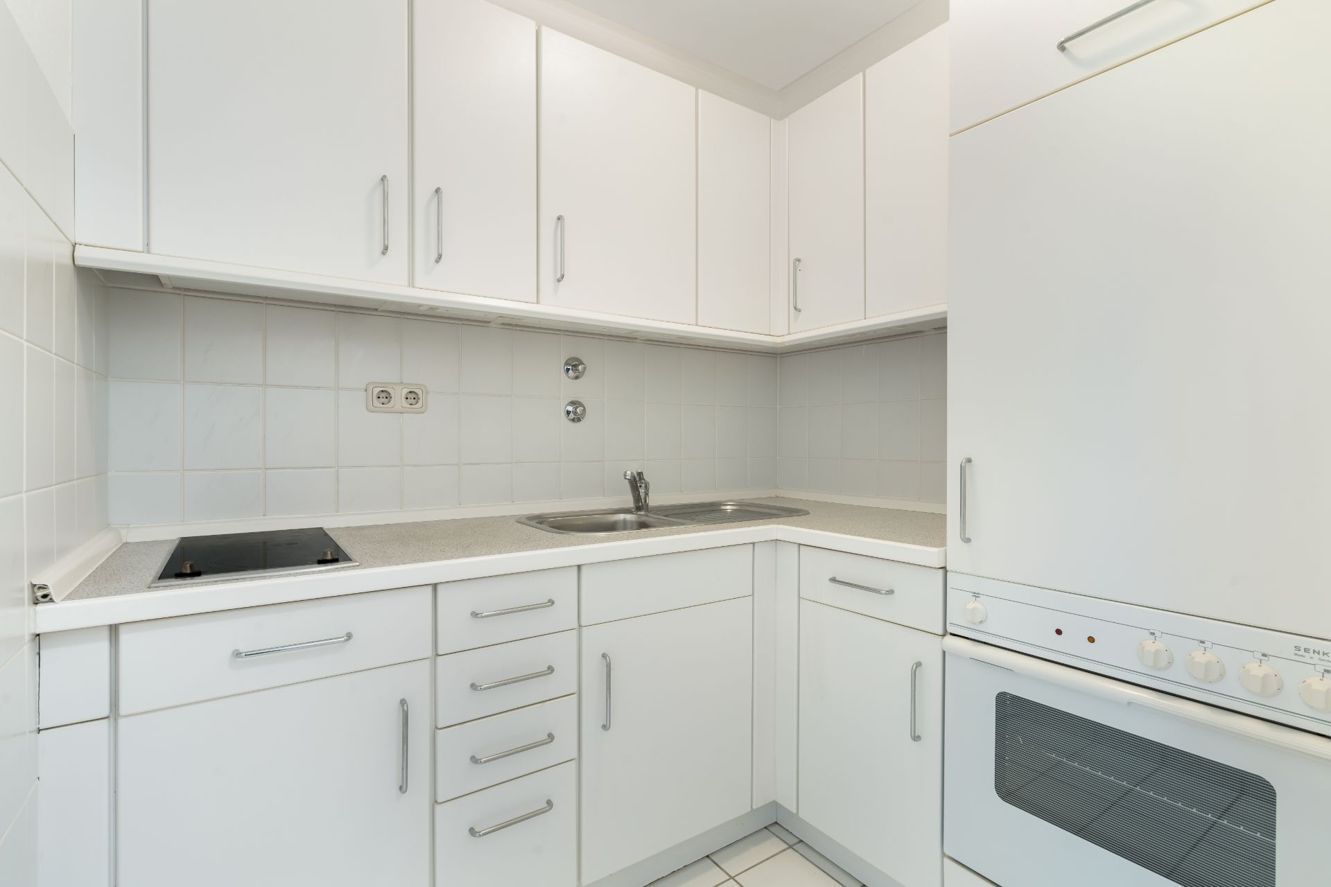 Moderne, weiße Einbauküche mit Herd, Spüle, Backofen und vielen Schränken.