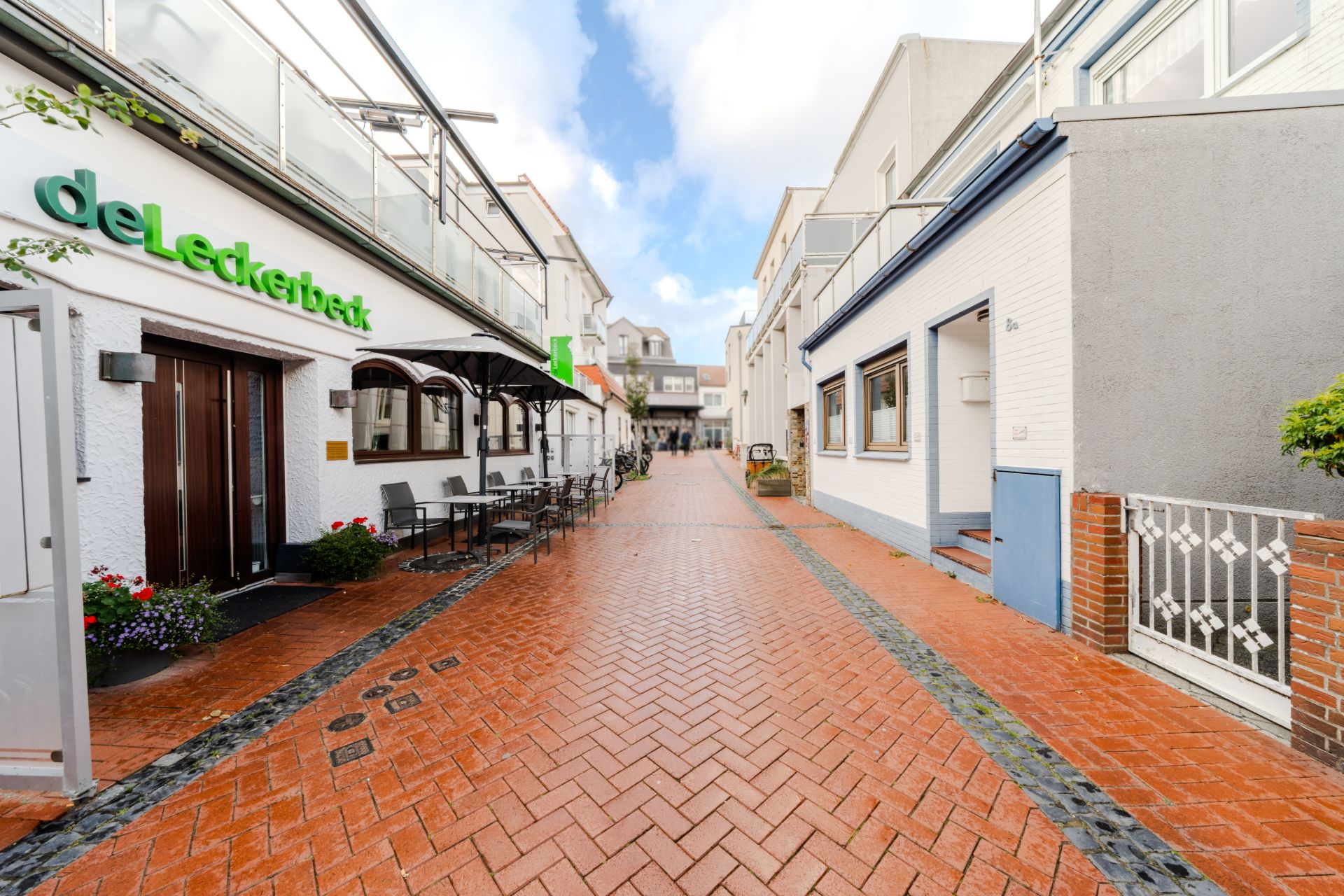 Schmale gepflasterte Gasse mit Sitzplätzen und weißen Wohngebäuden auf beiden Seiten.