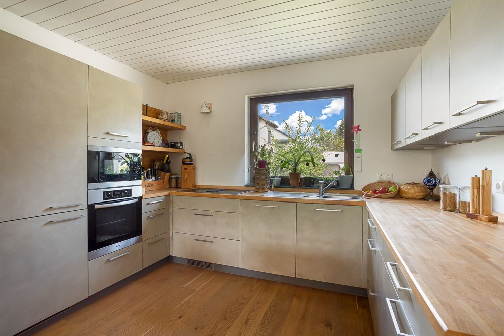Moderne Einbauküche mit Holzarbeitsfläche, großem Fenster und Haushaltsgeräten.