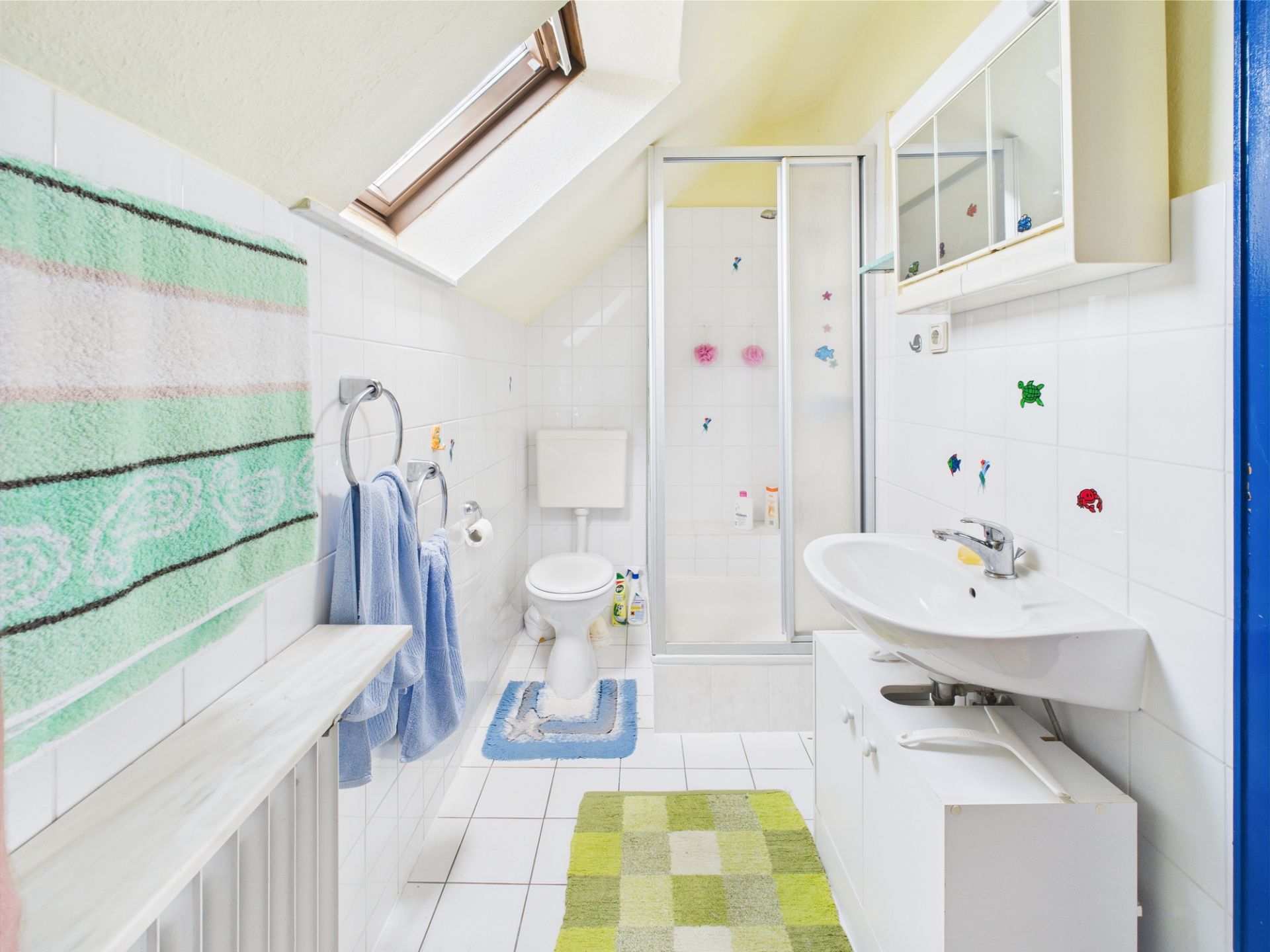 Helles Badezimmer mit Dachfenster, Dusche, Toilette, Waschbecken und bunten Handtüchern.