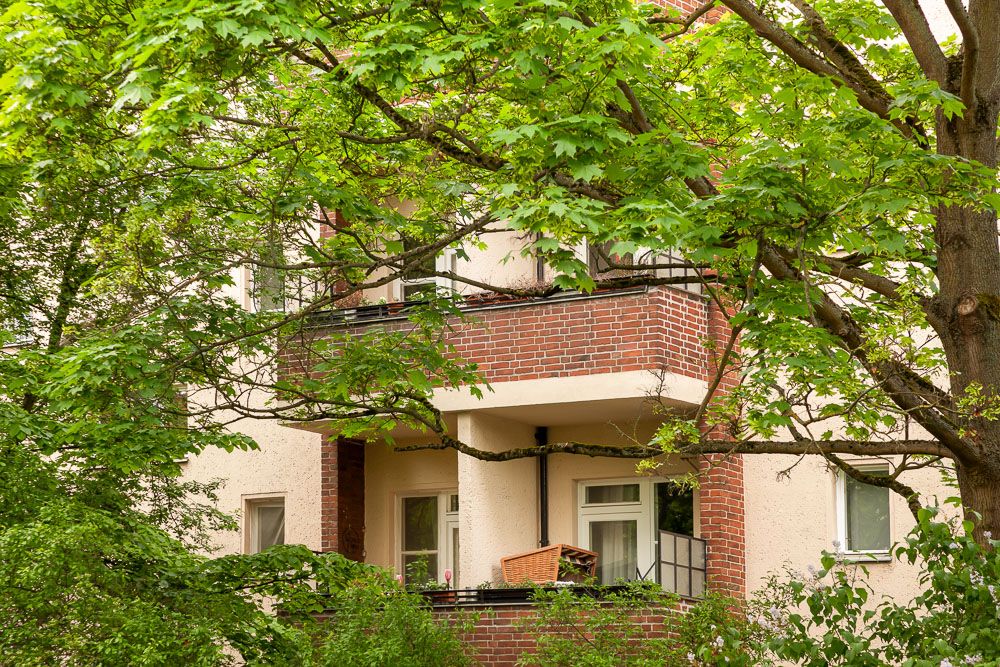 Balkon eines Wohngebäudes, teilweise von grünen Bäumen verdeckt.