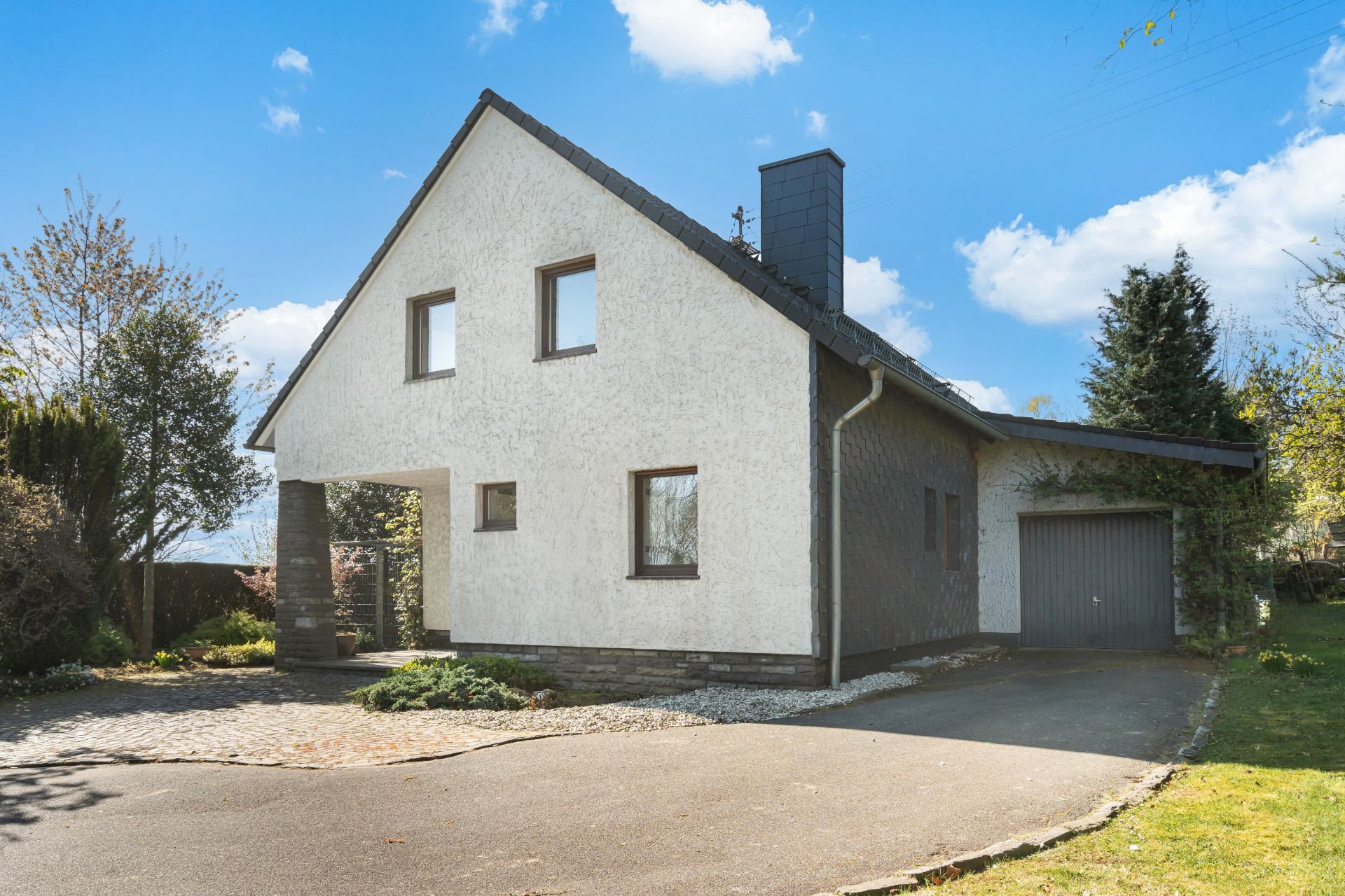 Zweistöckiges Wohnhaus mit Satteldach, Garage und Garten unter blauem Himmel.