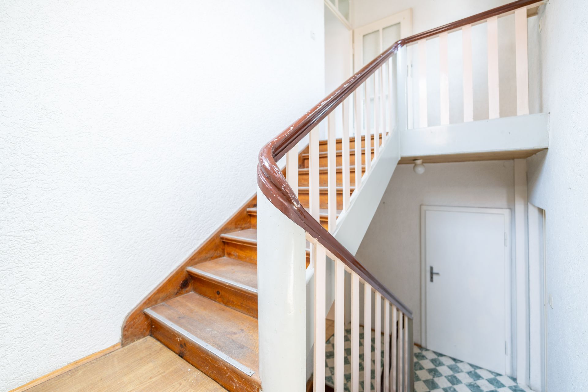 Helle Holztreppe mit weißem Geländer in einem Wohnhausflur, Tür unter der Treppe.