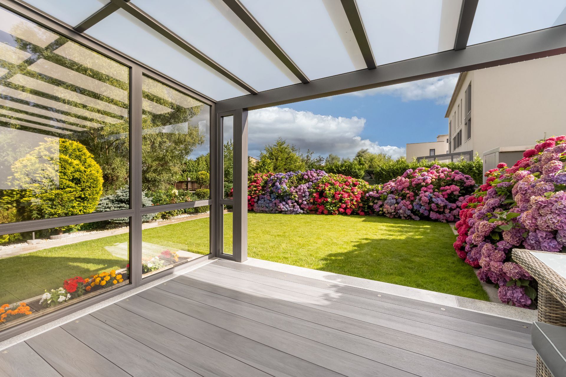 Überdachte Terrasse mit Holzboden, Blick auf grünen Garten und bunte Hortensiensträucher.