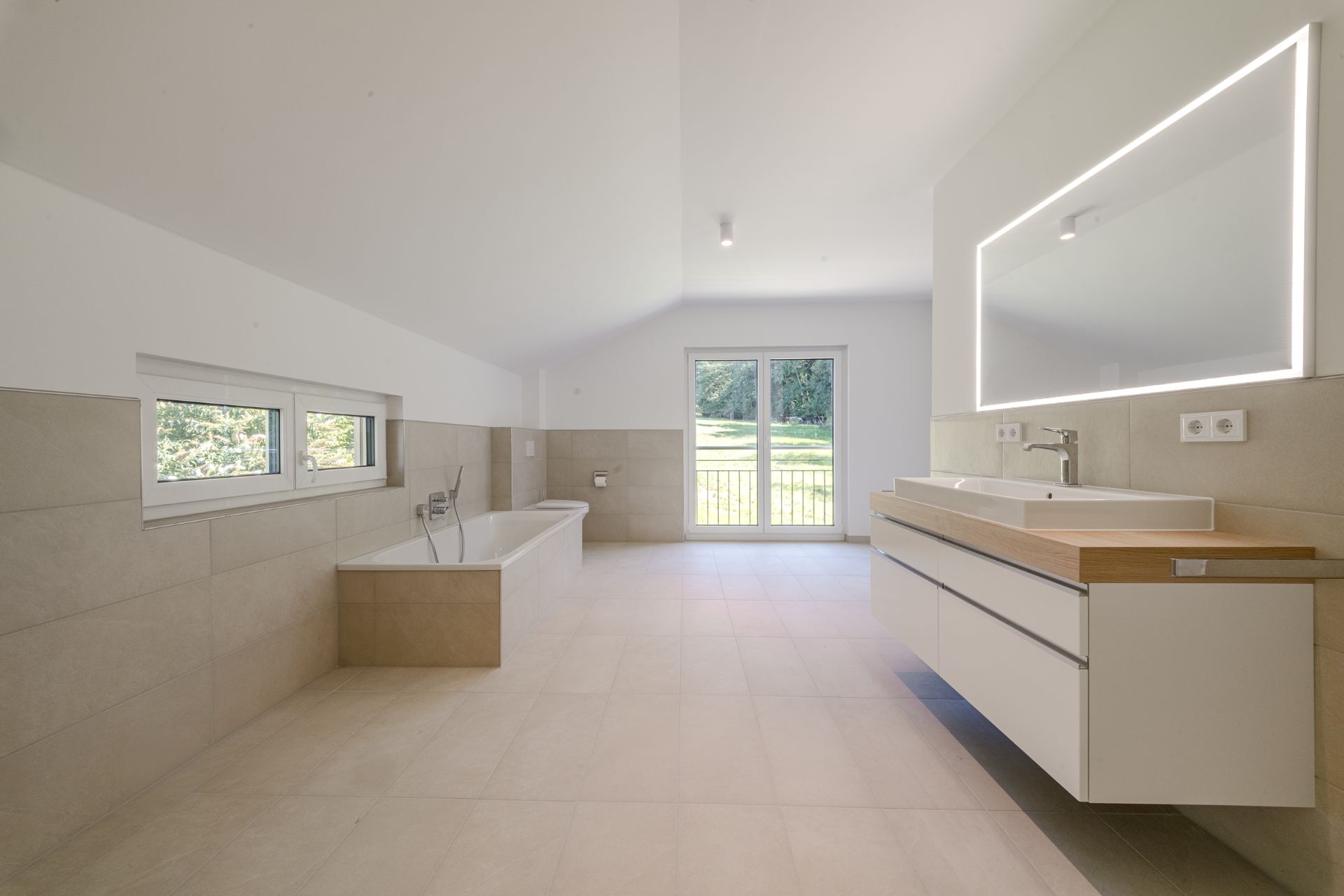 Modernes, helles Badezimmer mit Badewanne, Doppelwaschtisch und großem Fenster mit Blick ins Grüne.