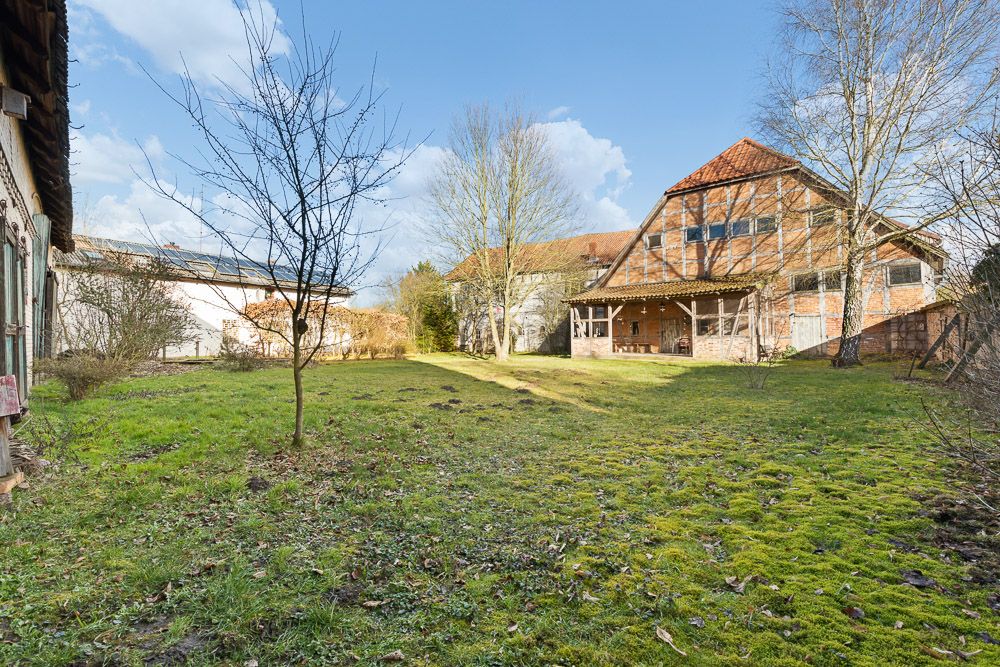 Großer grüner Garten mit Bäumen, Rasen und einem Fachwerkhaus im Hintergrund.