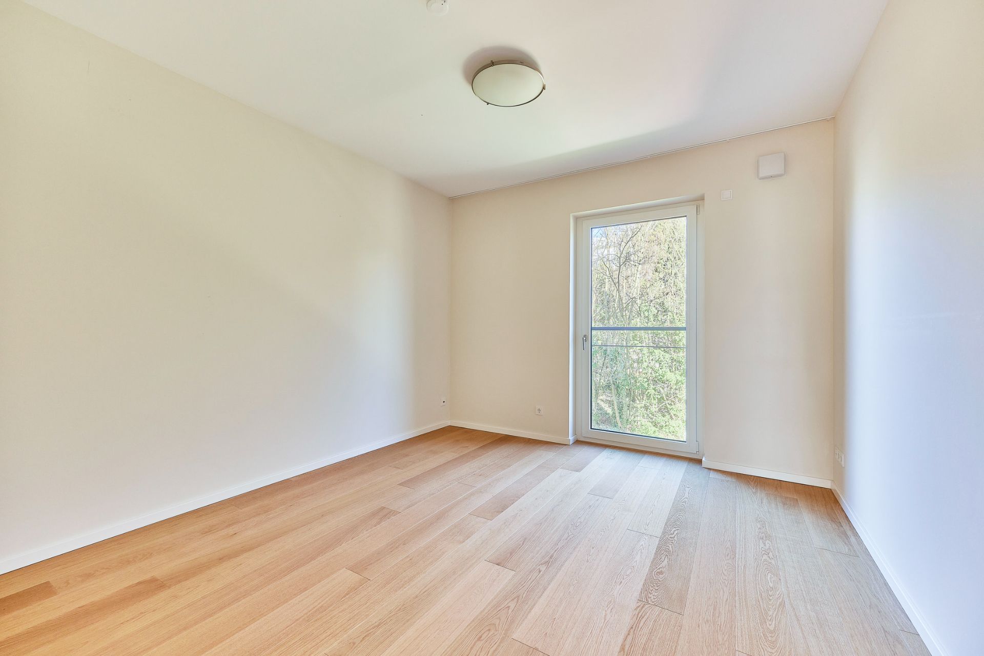 Leerer Raum mit Holzboden, weißen Wänden und großer Fenster-Tür zum Balkon.