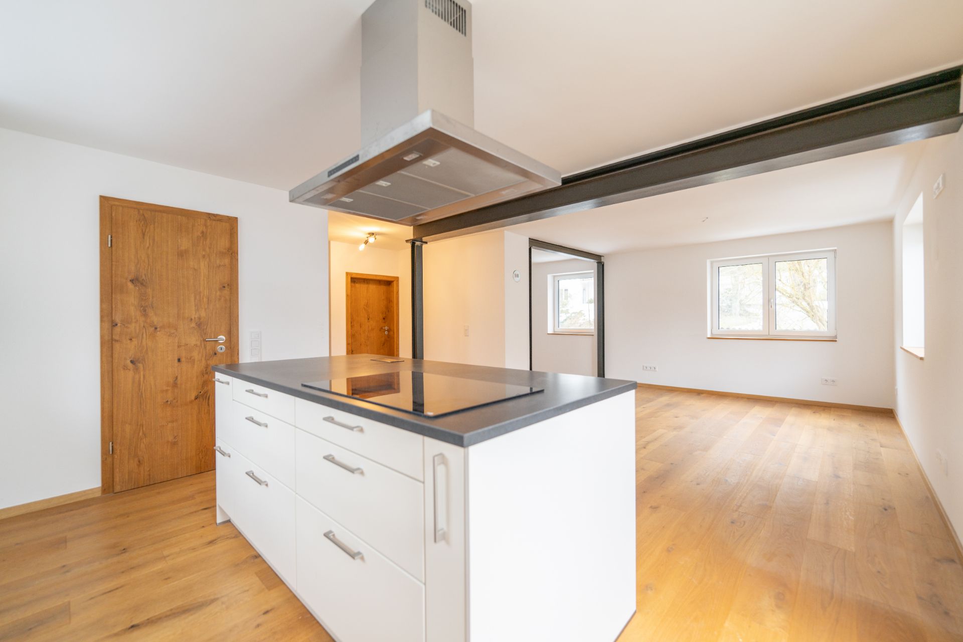 Moderne offene Küche mit Kochinsel und angrenzendem Wohnbereich, Parkettboden, große Fenster.