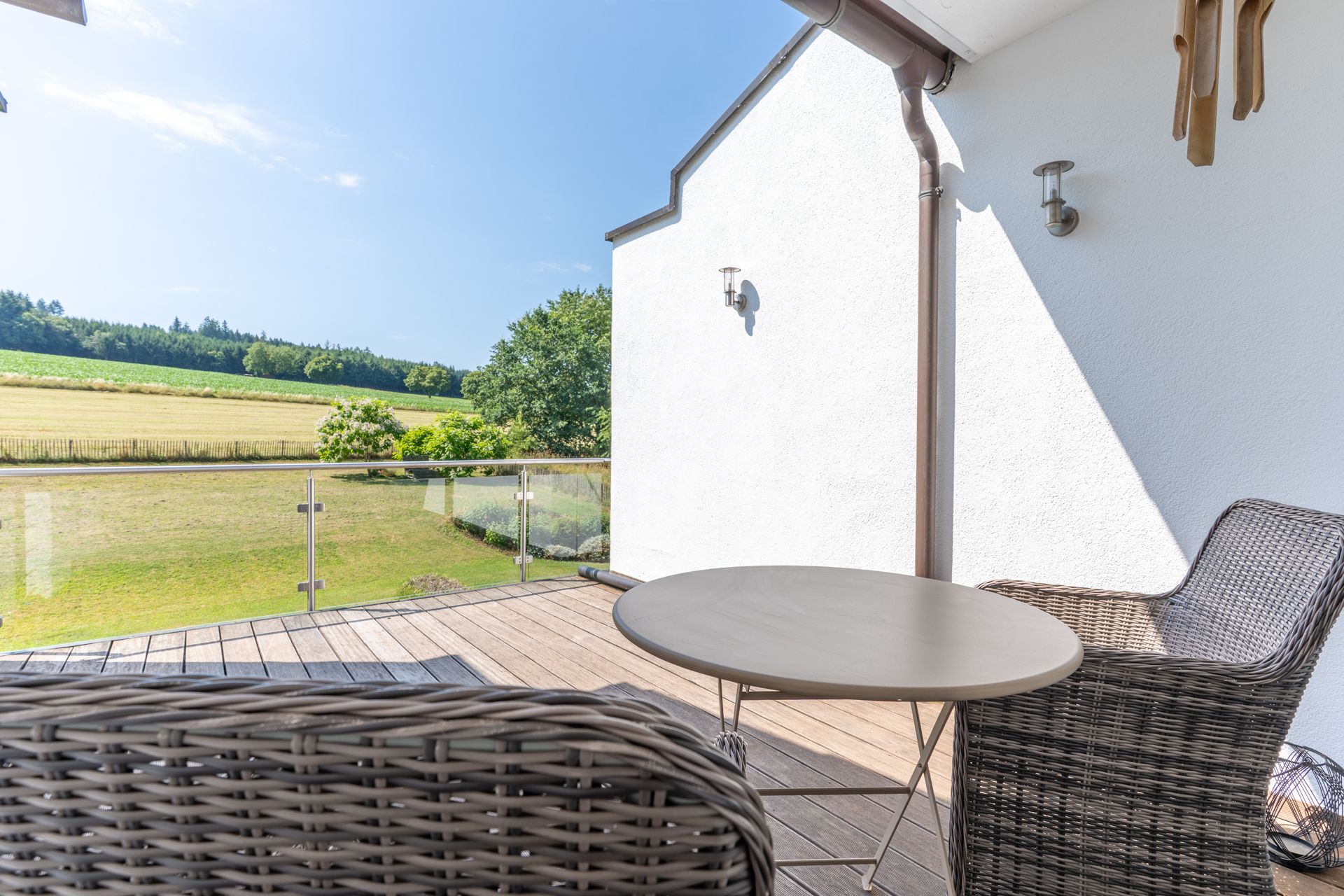 Balkon mit zwei Korbstühlen und rundem Tisch, Blick auf Wiese und Bäume.