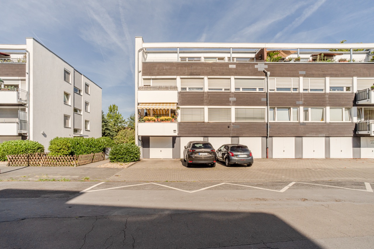Mehrfamilienhaus mit Garagen und zwei geparkten Autos vor dem Gebäude.