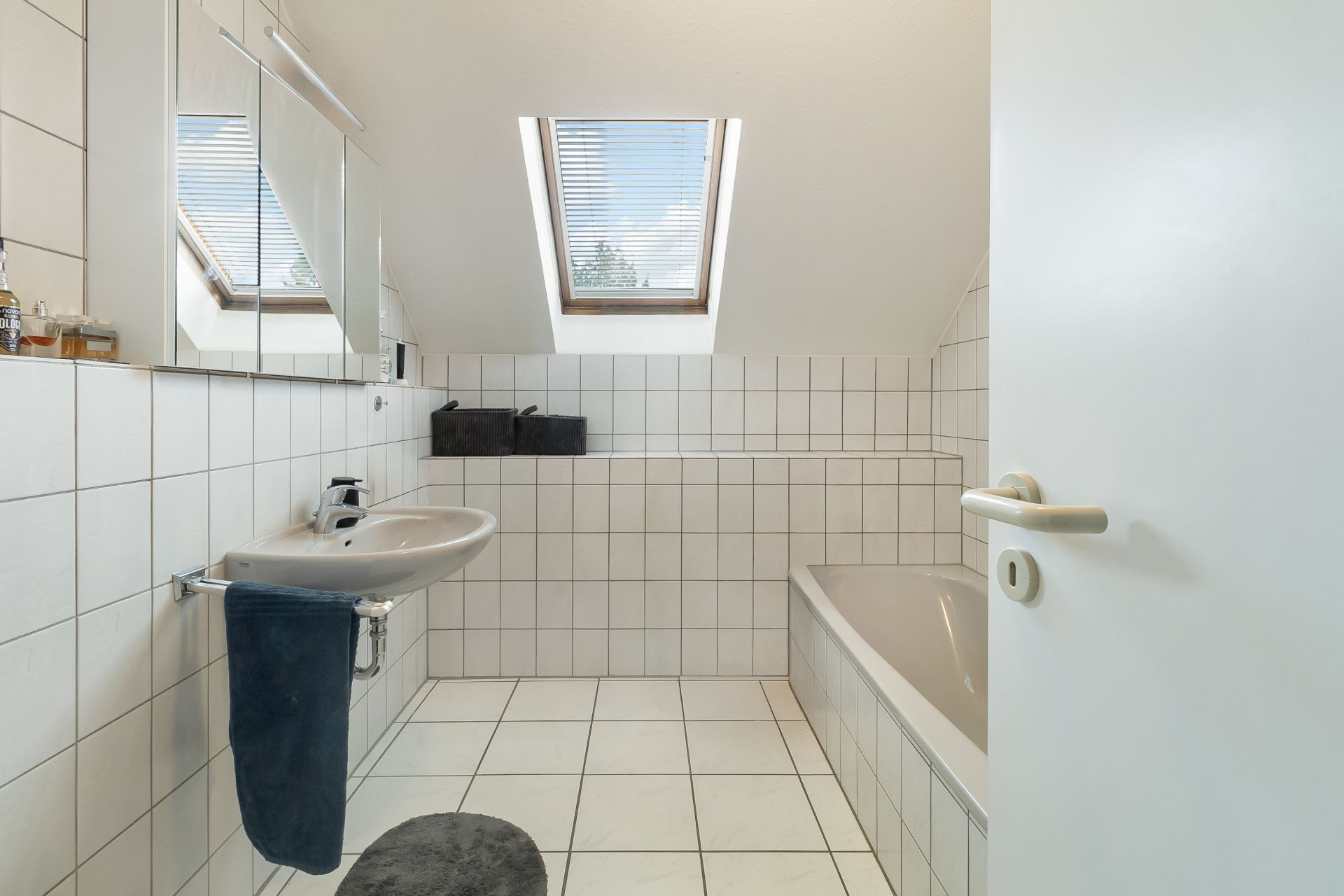 Helles Badezimmer mit Badewanne, Waschbecken, Wandspiegel und Dachfenstern.