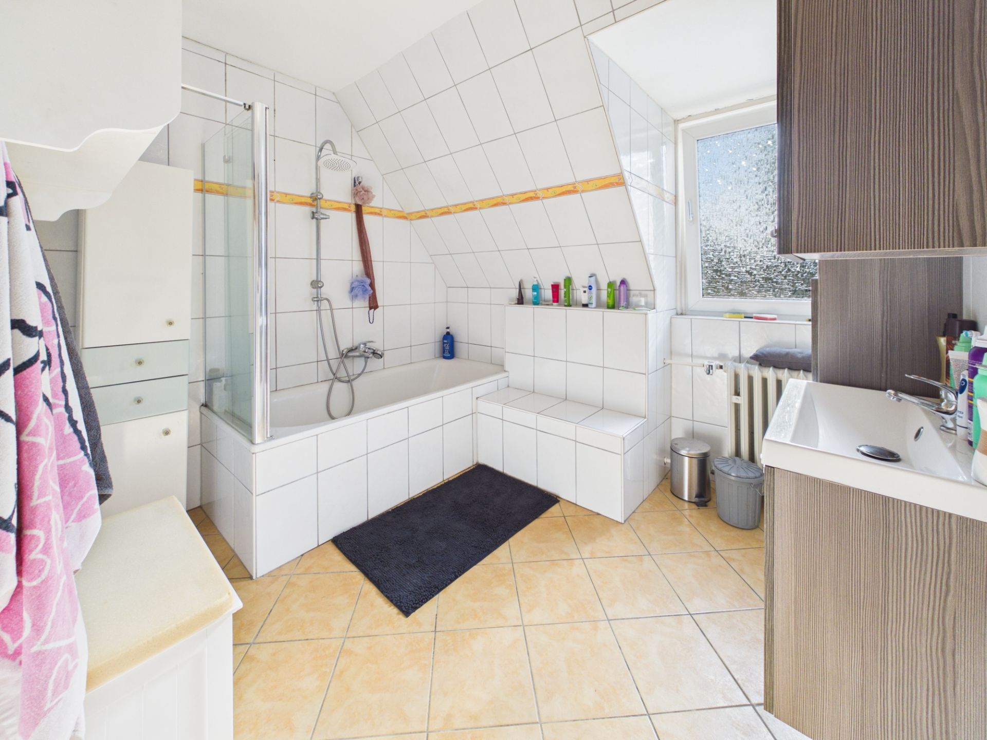Helles Badezimmer mit Badewanne, Waschbecken, Fenster und Fliesenboden.