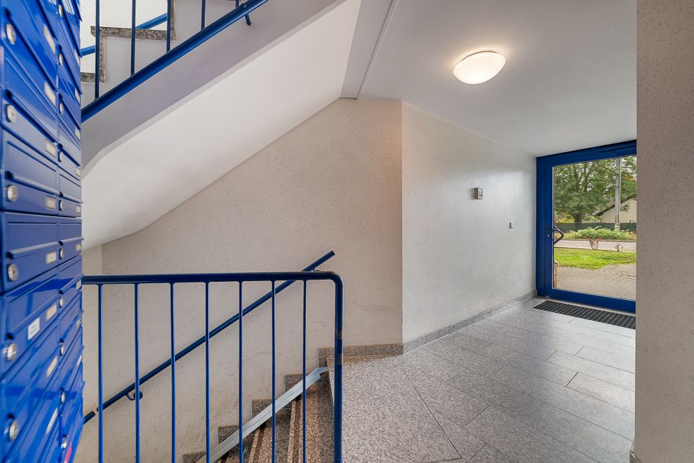 Eingangsbereich eines Wohnhauses mit Briefkästen, Treppe und Glastür zum Außenbereich.