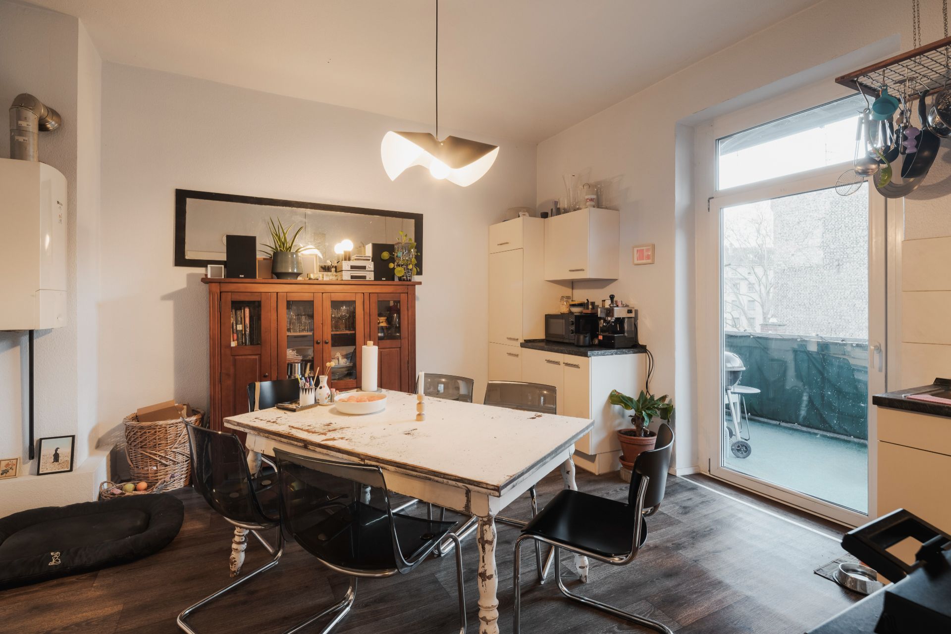 Esszimmer mit weißem Tisch, schwarzen Stühlen, Holzschrank und Zugang zu einem Balkon.