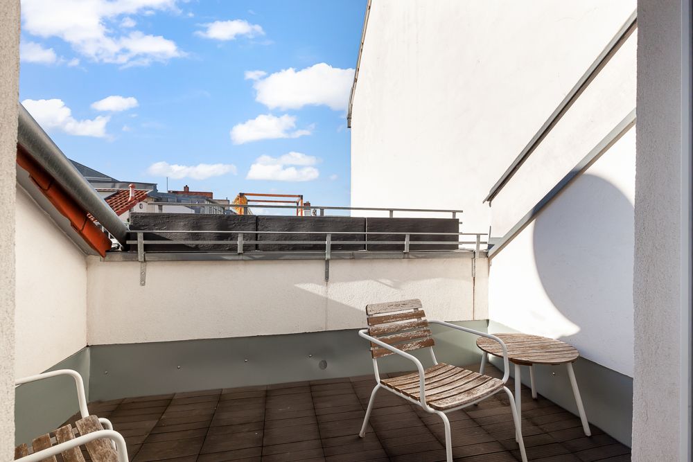Kleine Dachterrasse mit zwei Holzstühlen und einem runden Holztisch.