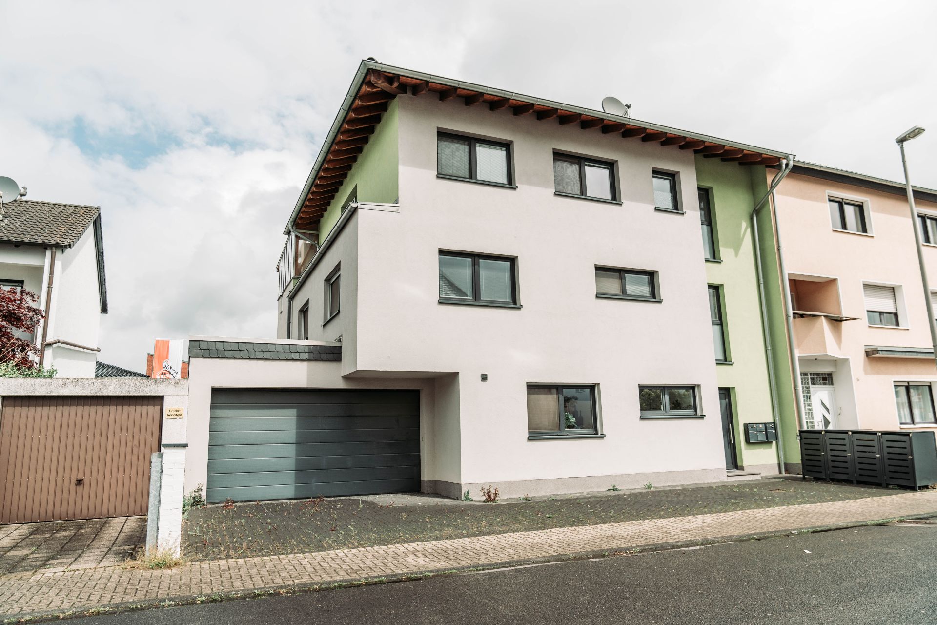 Modernes, dreistöckiges Wohnhaus mit Garage und mehreren Fenstern an der Straßenseite.