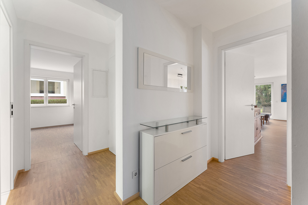 Heller Flur mit Holzfußboden, Kommode und Wandspiegel, Türen führen in andere Zimmer.