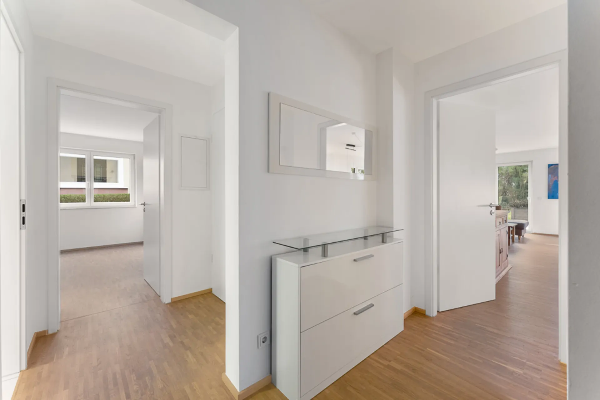 Heller Flur mit Holzfußboden, Kommode und Wandspiegel, Türen führen in andere Zimmer.