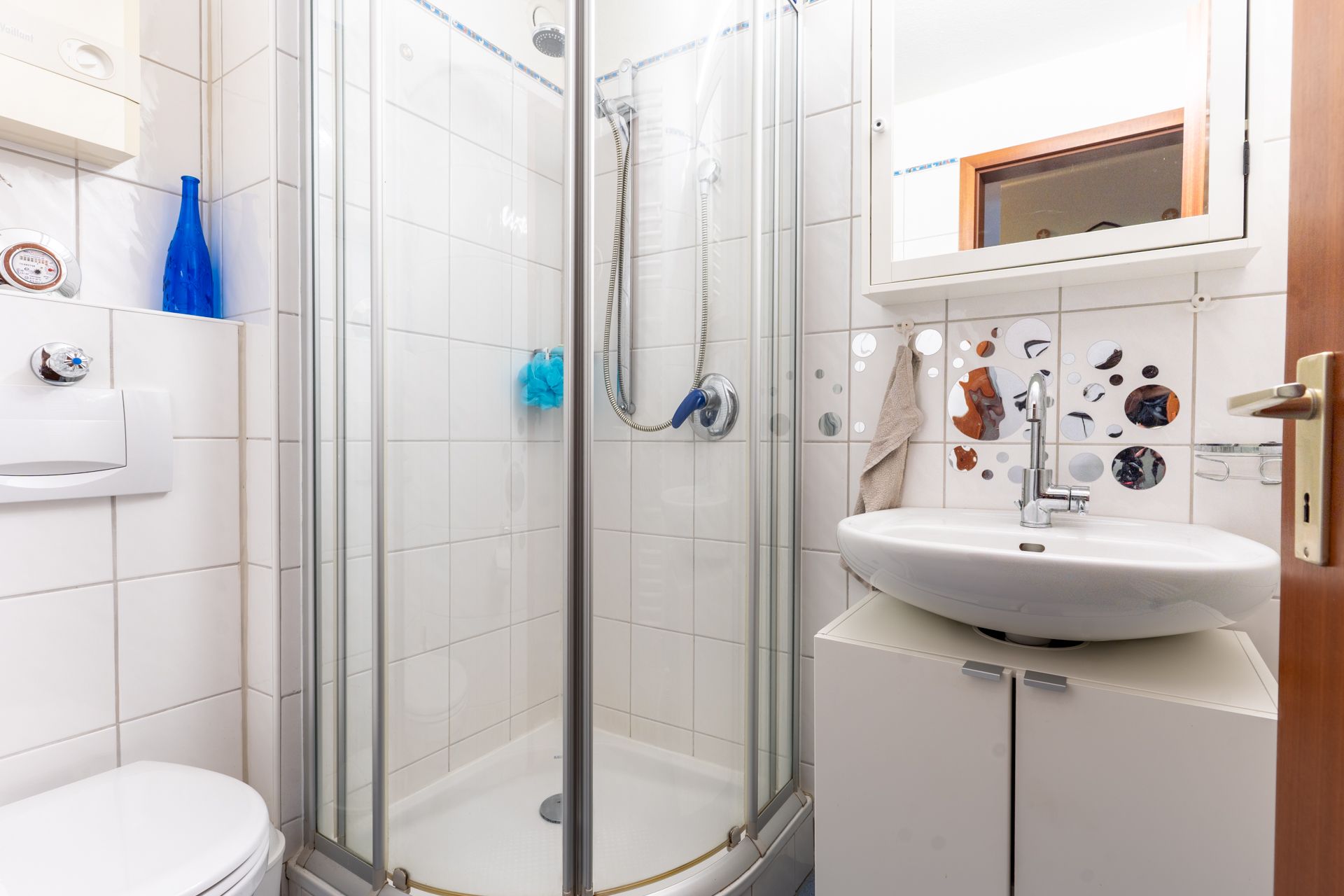 Kleines Badezimmer mit Dusche, Waschbecken und Spiegel.
