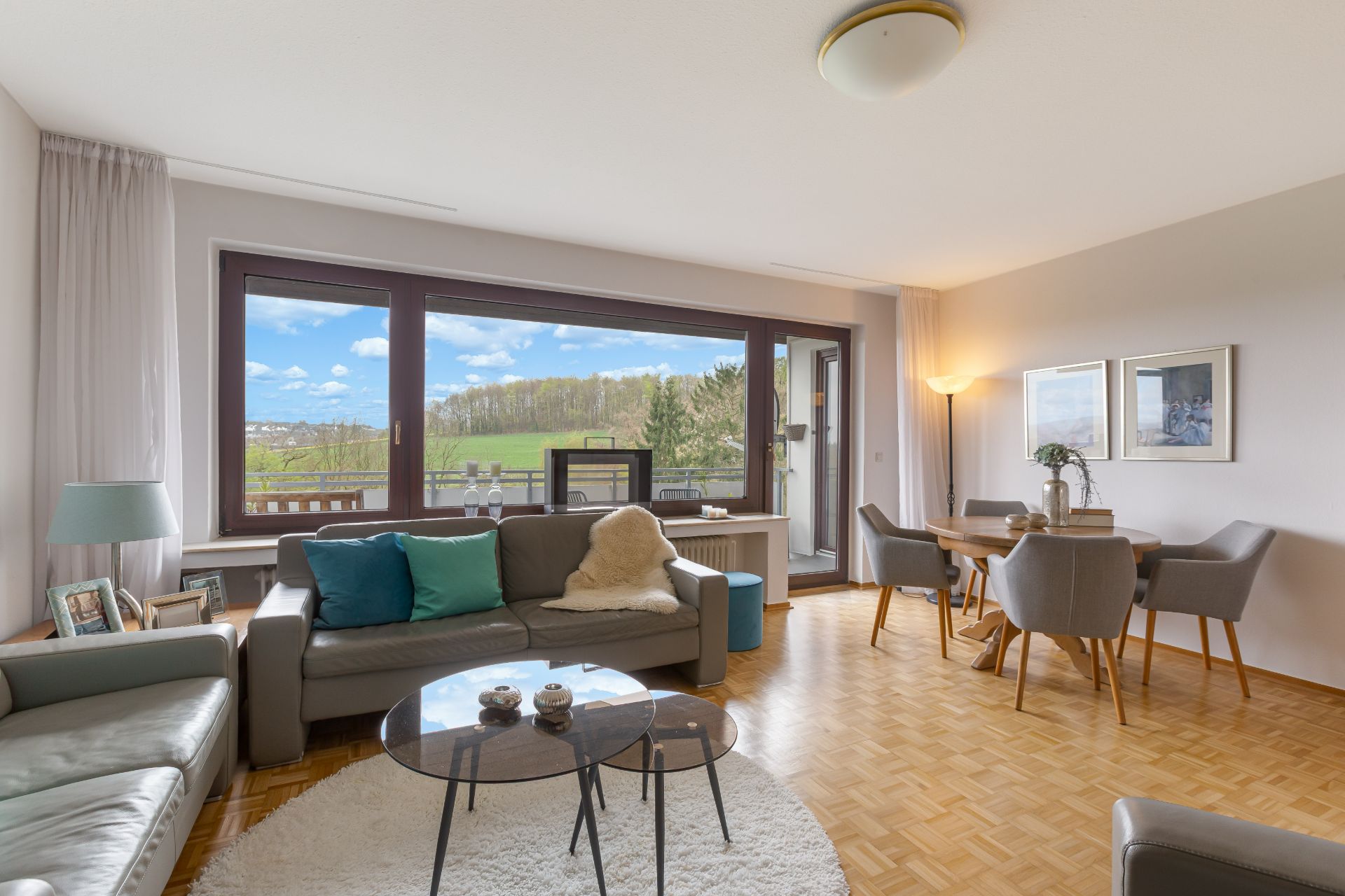 Modernes Wohnzimmer mit großen Fenstern, Sofas, Couchtischen und einem Esstisch mit Stühlen.