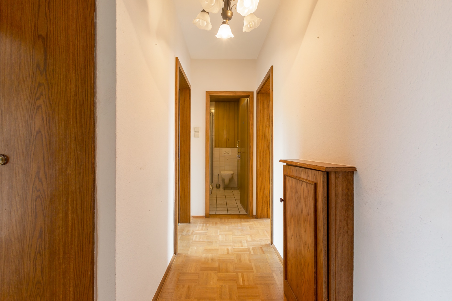 Heller Flur mit Holztüren, Holzschrank und Blick auf ein Badezimmer mit WC.
