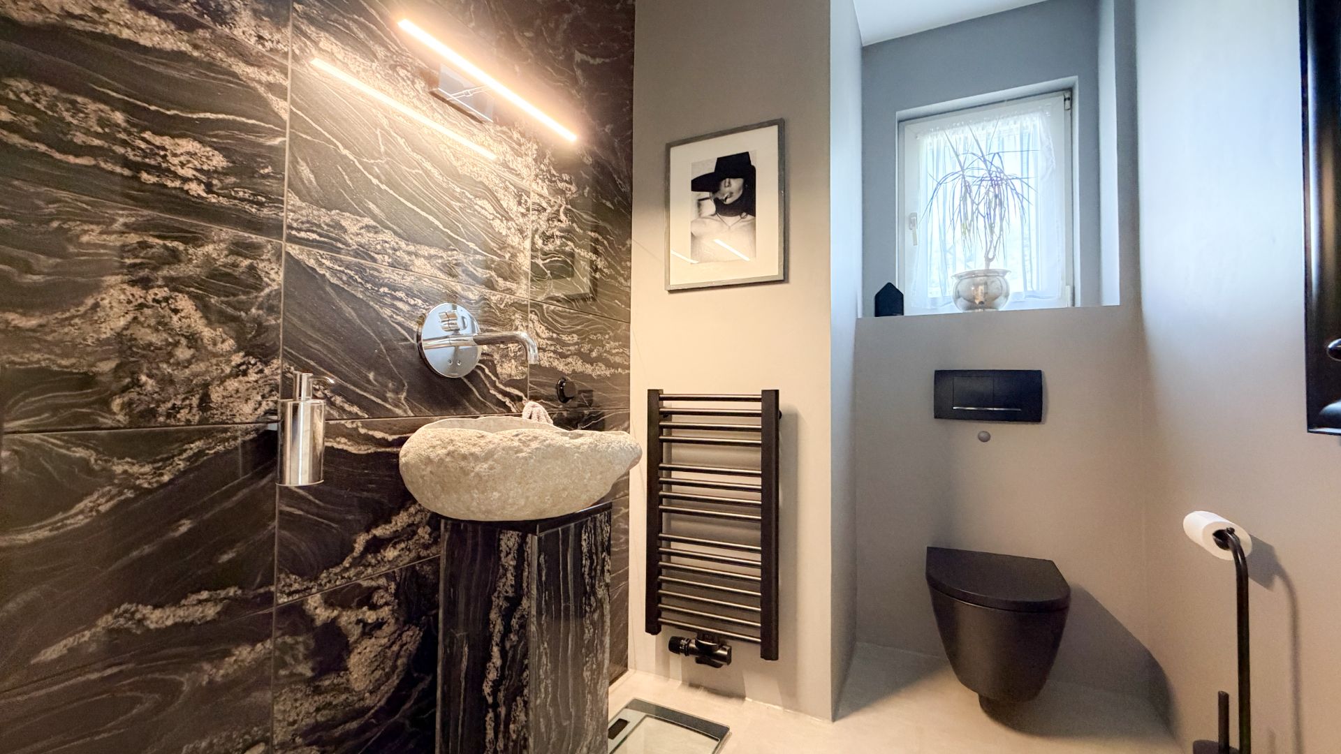 Modernes Badezimmer mit schwarzem Waschbecken, Toilette, Handtuchheizkörper und Fenster.
