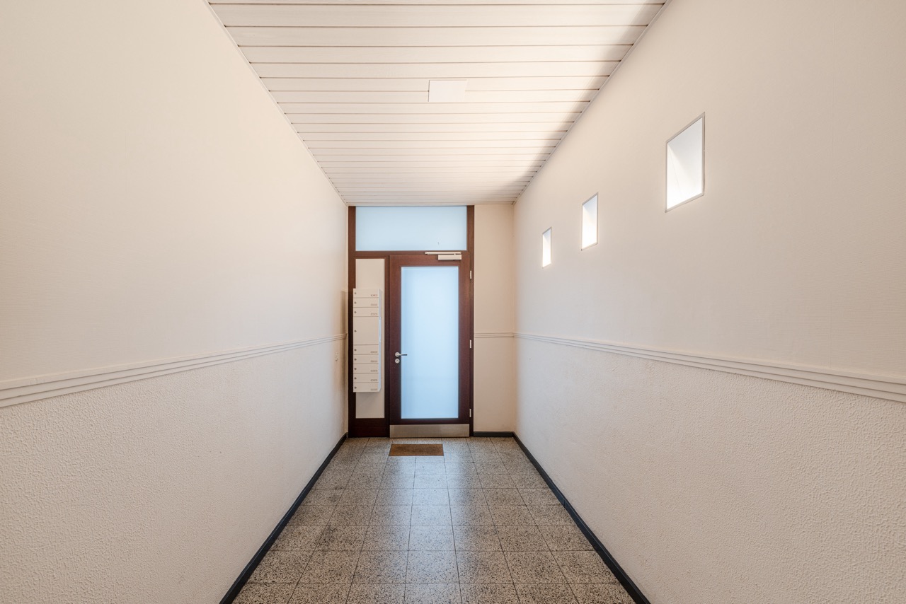 Heller Flur mit Fliesenboden, Briefkästen und Tür mit Milchglas in einem Wohnhaus.