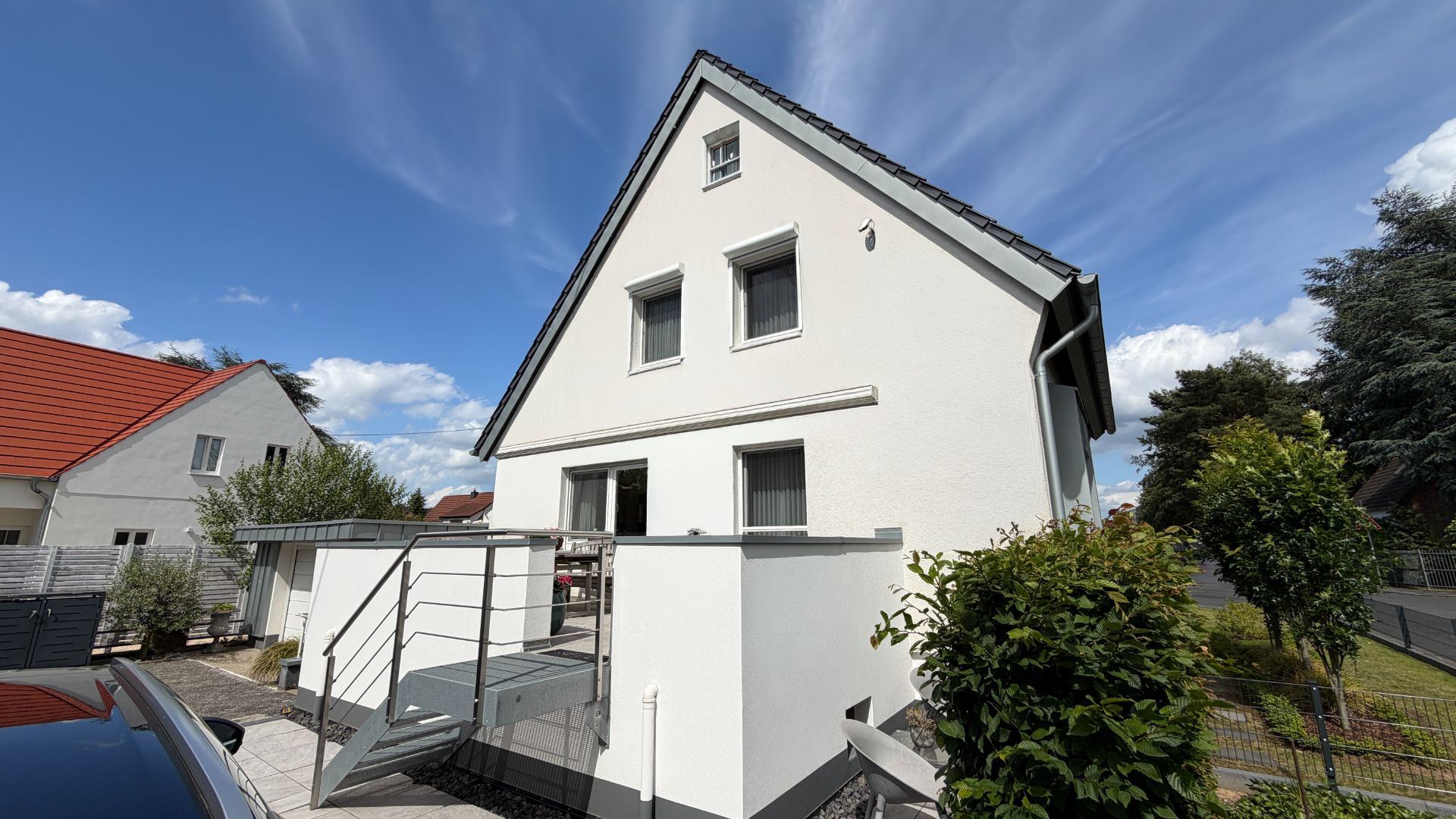 Modernes weißes Einfamilienhaus mit Garten, Terrasse und Außentreppe an sonnigem Tag.