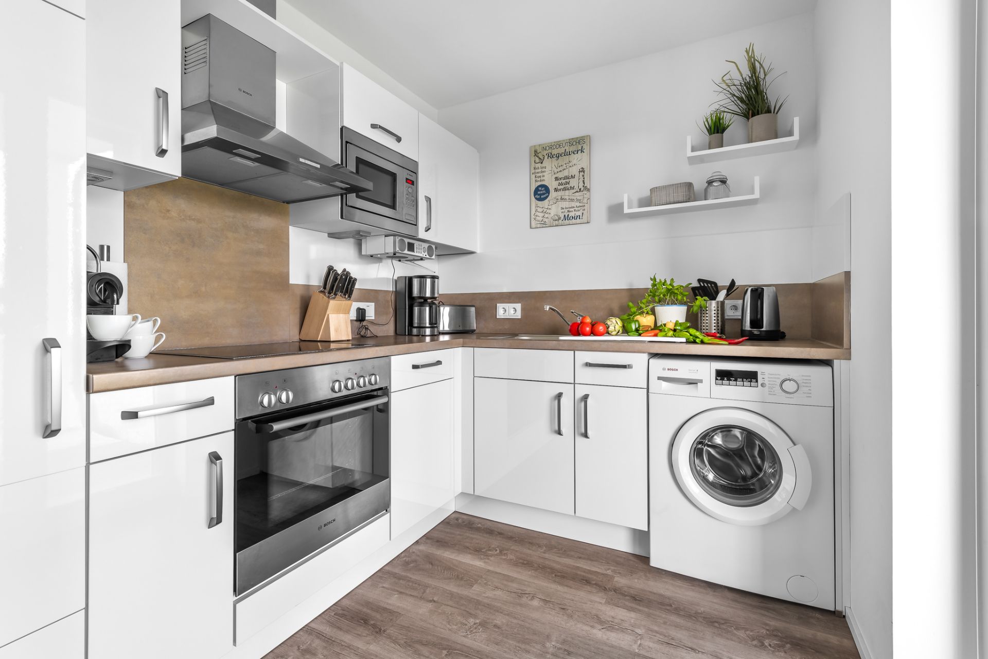 Moderne Einbauküche mit weißen Schränken, Elektrogeräten und Waschmaschine in einer Ecke.