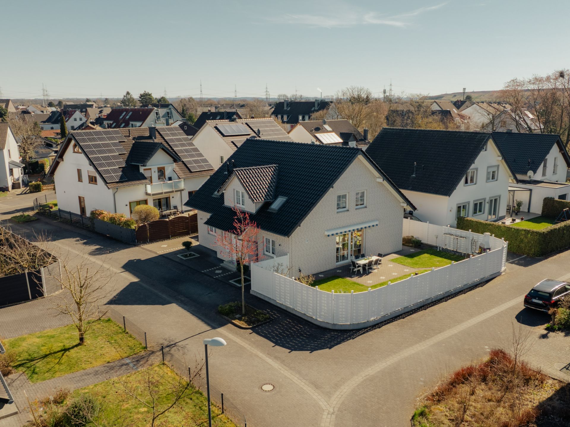 Luftaufnahme von Einfamilienhäusern mit Gärten und weißen Zäunen in einer Wohnsiedlung.