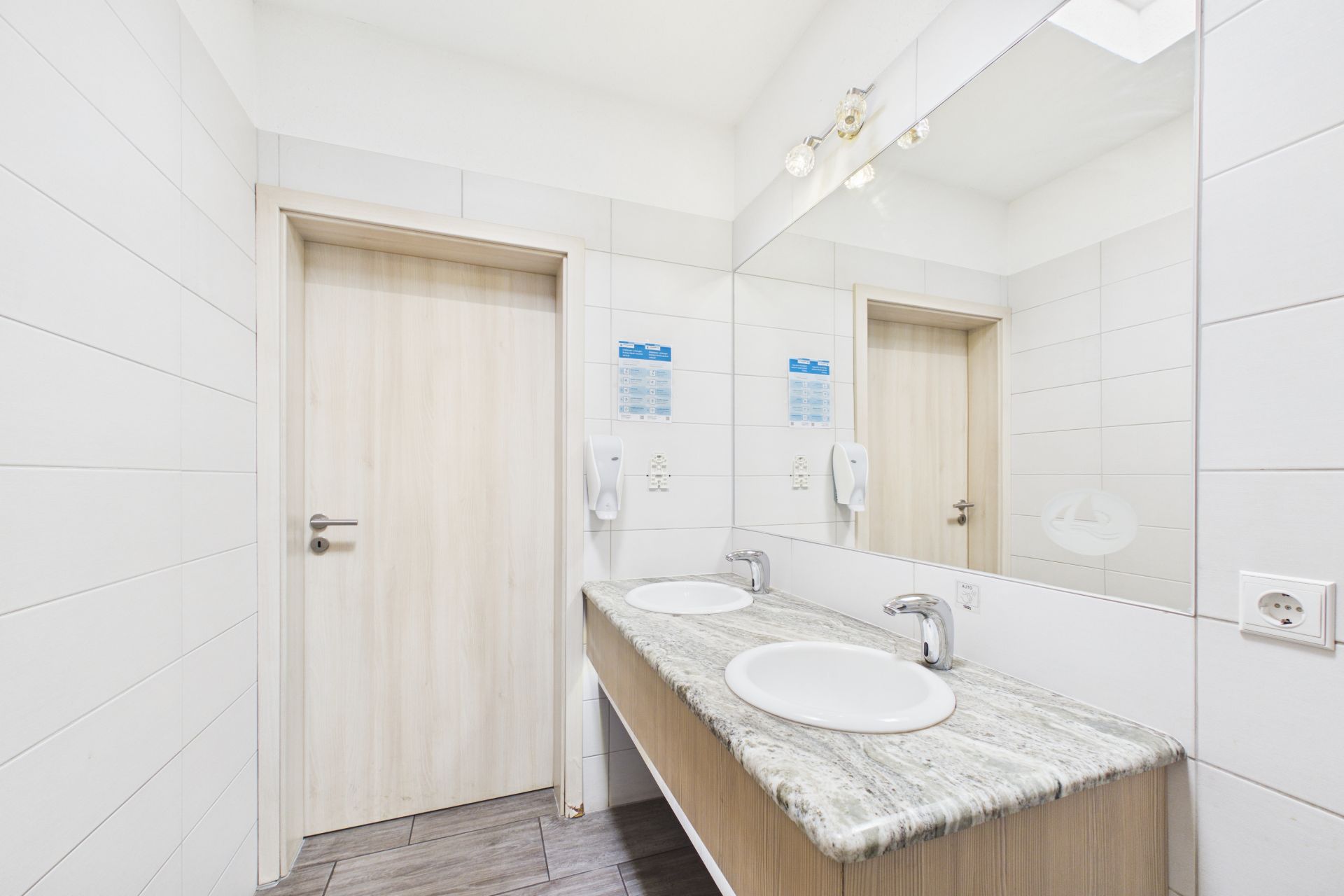 Helles Badezimmer mit zwei Waschbecken, großem Spiegel und zwei Holztüren.