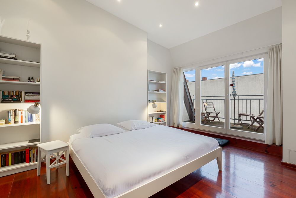 Helles Schlafzimmer mit Doppelbett, Bücherregalen und Zugang zu einem Balkon mit Stühlen.