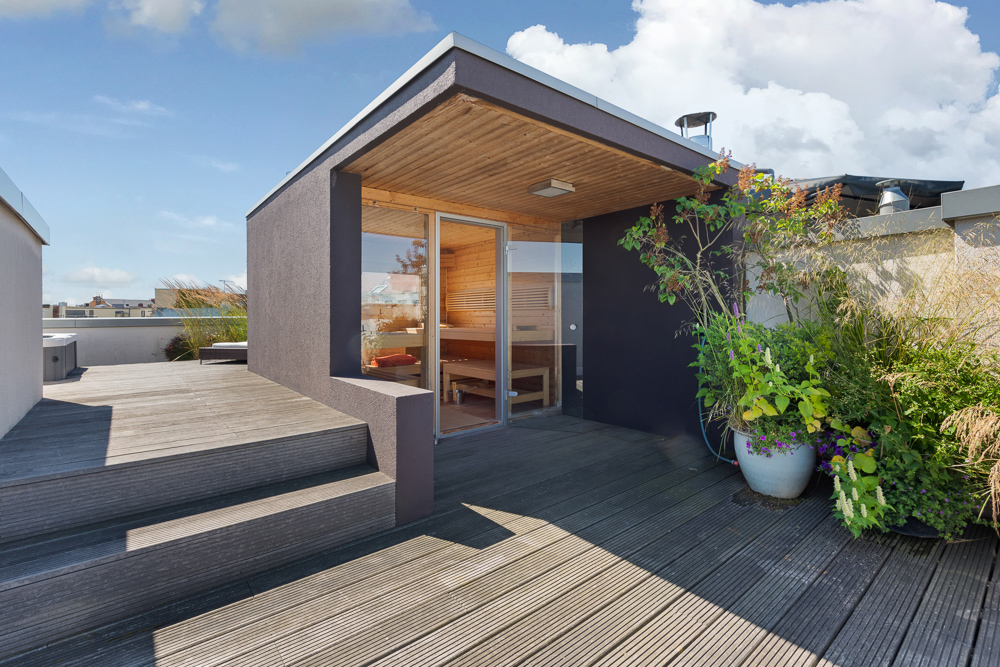 Dachterrasse mit Holzboden, kleinen Pflanzen und einem modernen Holzanbau mit Glasfront.
