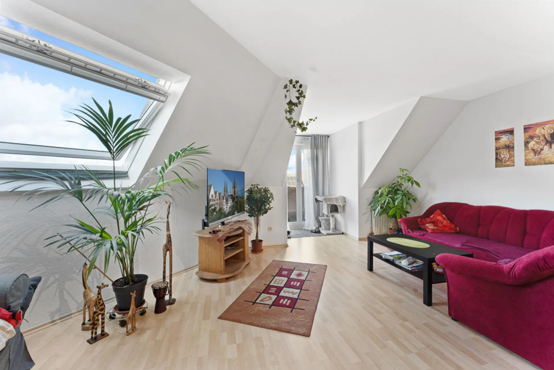Helles Wohnzimmer mit Dachfenster, roten Sofa, Pflanzen, Fernseher und Teppich.