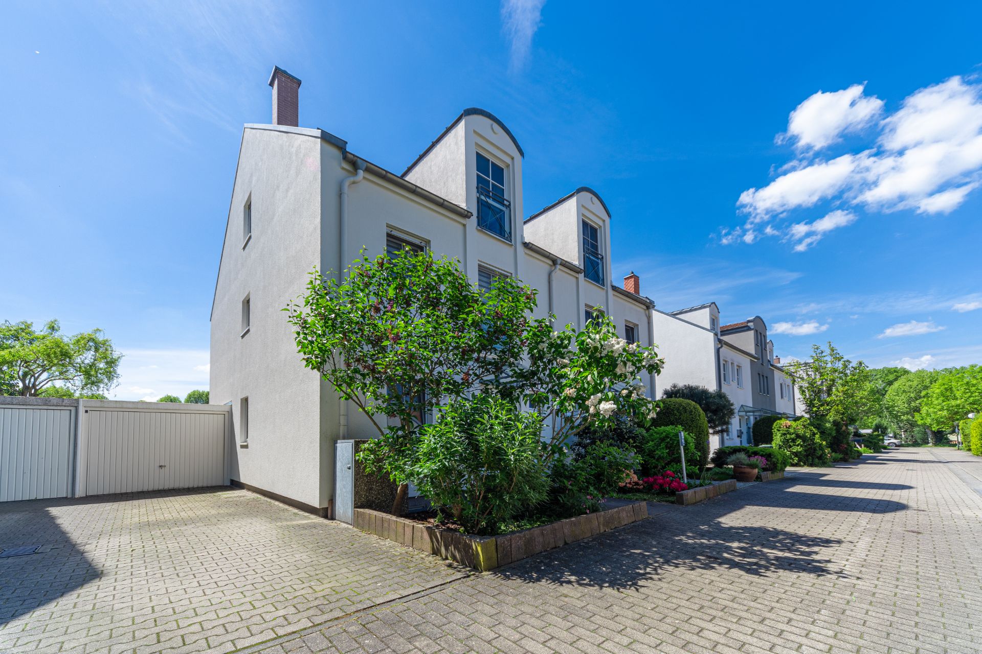 Modernes Wohnhaus mit Vorgarten, Pflasterhof und blauem Himmel.
