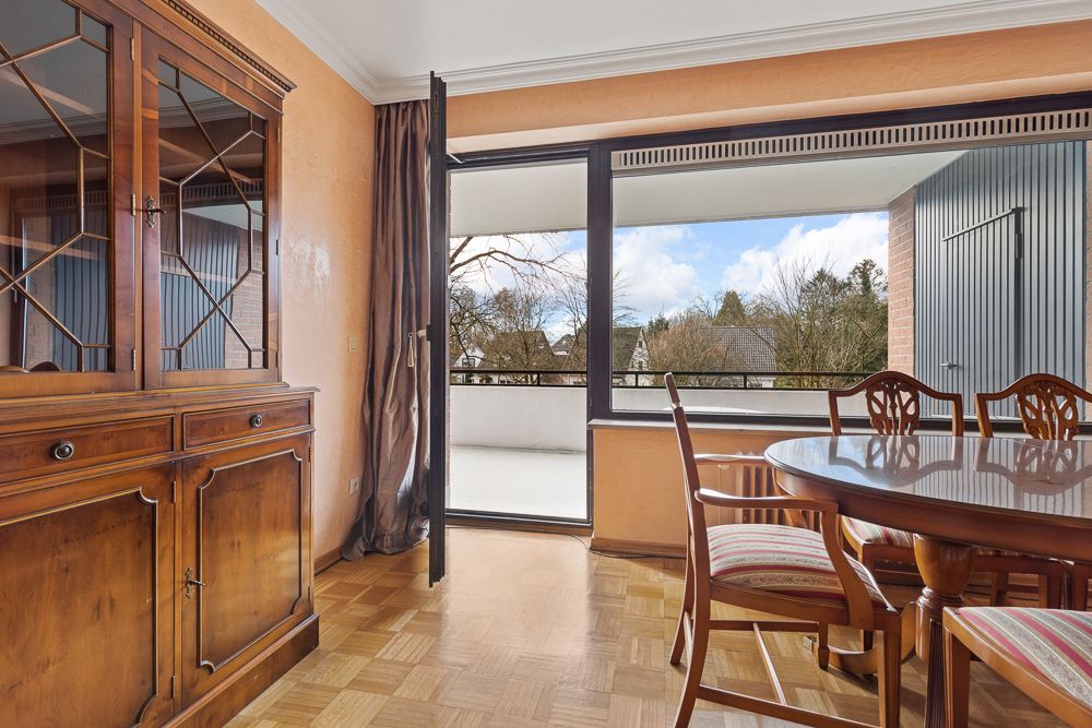 Esszimmer mit Holzmöbeln und Zugang zu einem Balkon mit Ausblick ins Grüne.