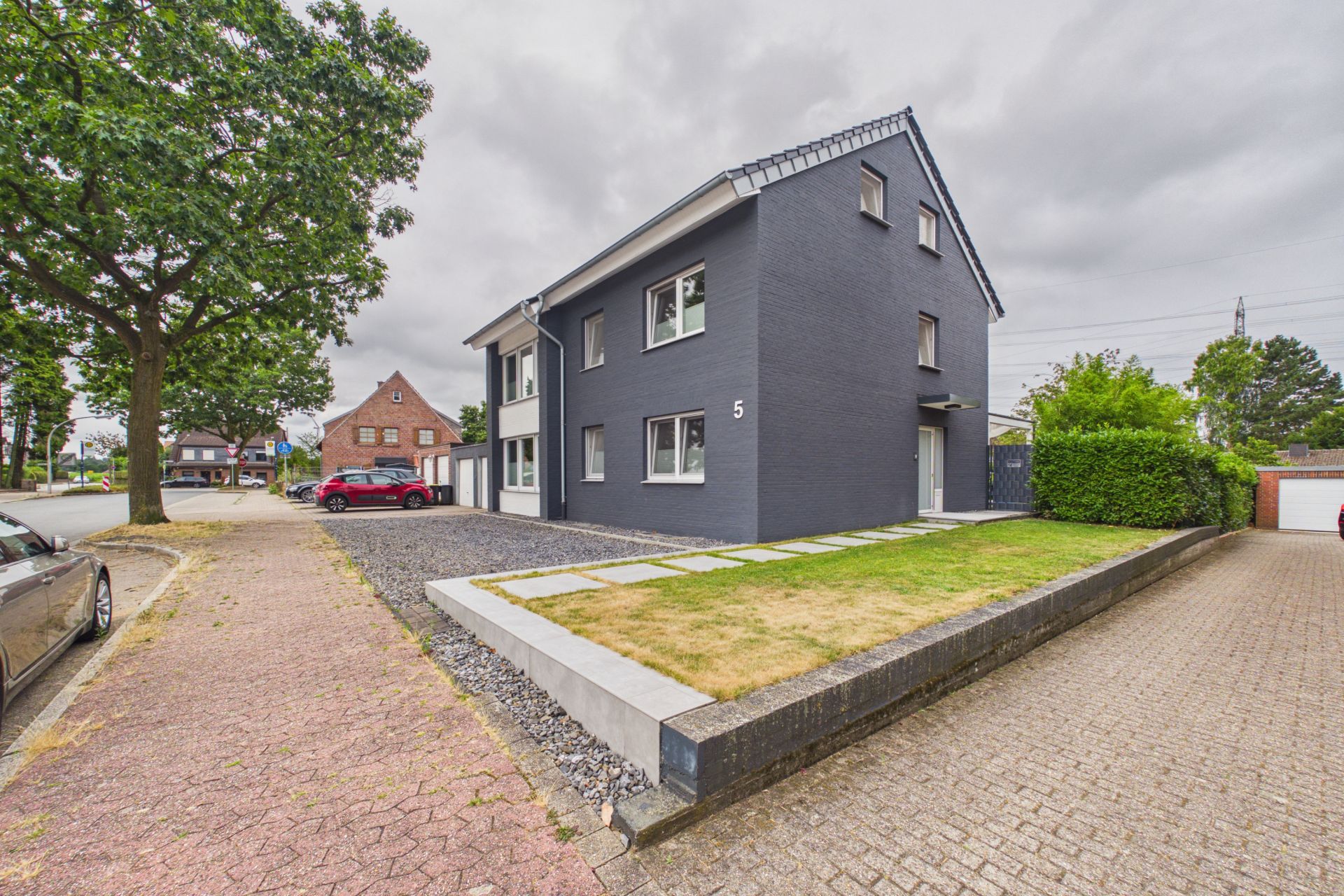 Modernes, dunkelgraues Wohnhaus mit Vorgarten und gepflasterter Einfahrt.