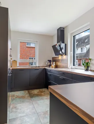 Moderne Küche mit dunklen Schränken, Holzarbeitsplatte und zwei Fenstern.