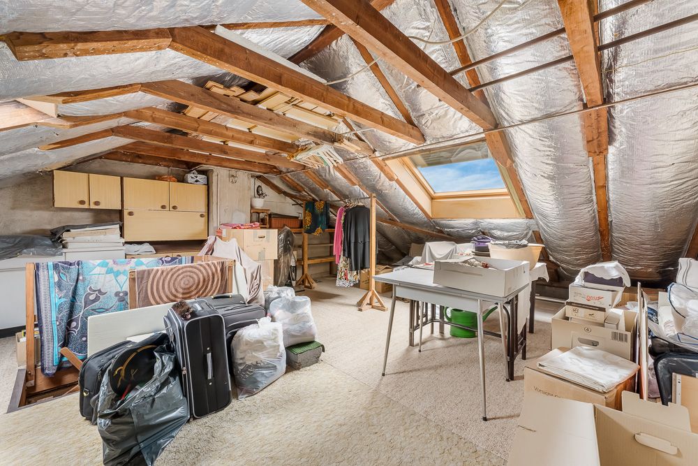 Ein Dachboden mit sichtbaren Holzbalken, Dachfenster und verschiedenen gelagerten Gegenständen.