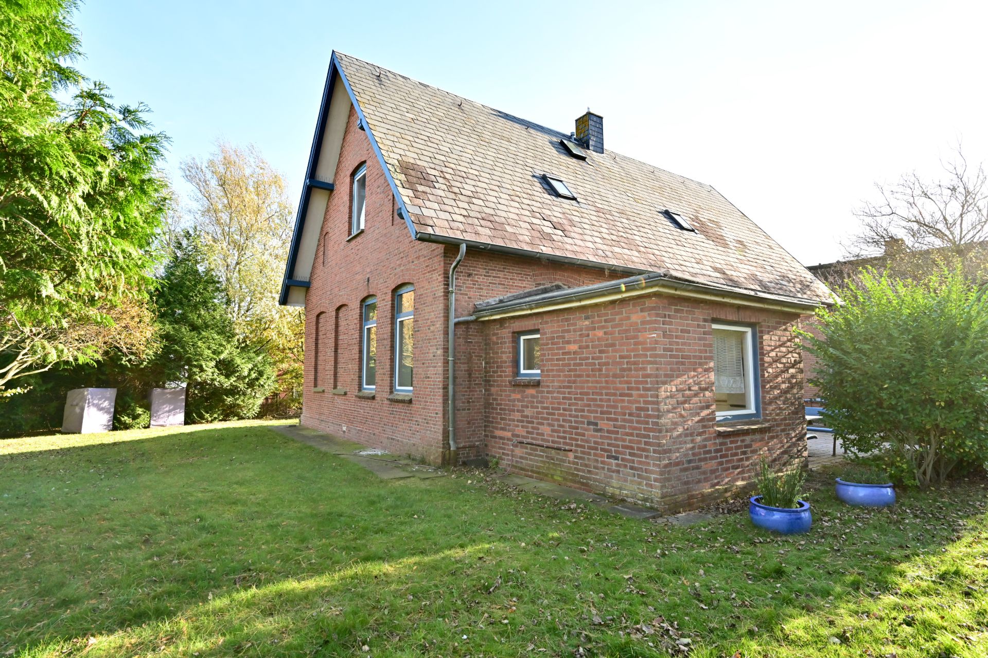 Backsteinwohnhaus mit großem Garten und blauen Blumentöpfen neben dem Haus.