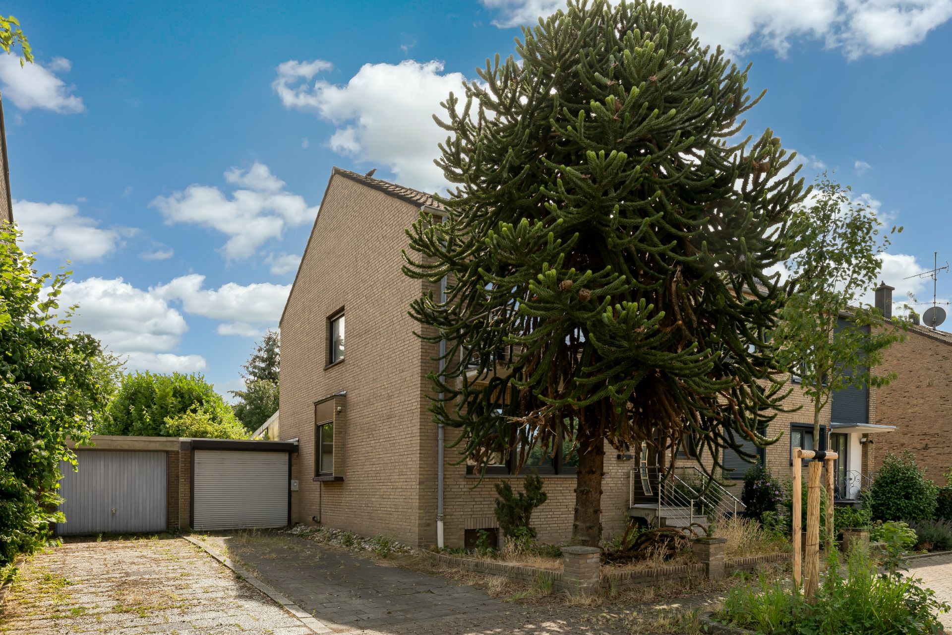 Zweistöckiges Wohnhaus mit großem Baum im Vorgarten und Garage rechts im Bild.