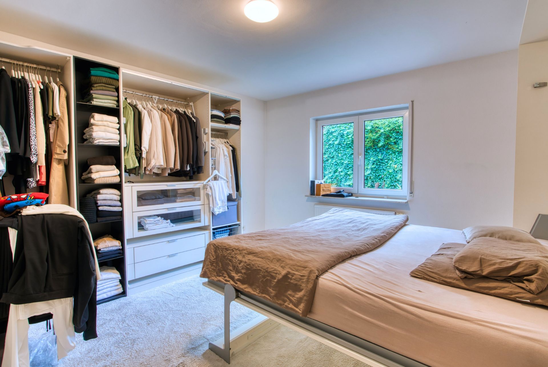 Schlafzimmer mit Doppelbett, offenem Kleiderschrank und Fenster mit Blick ins Grüne.
