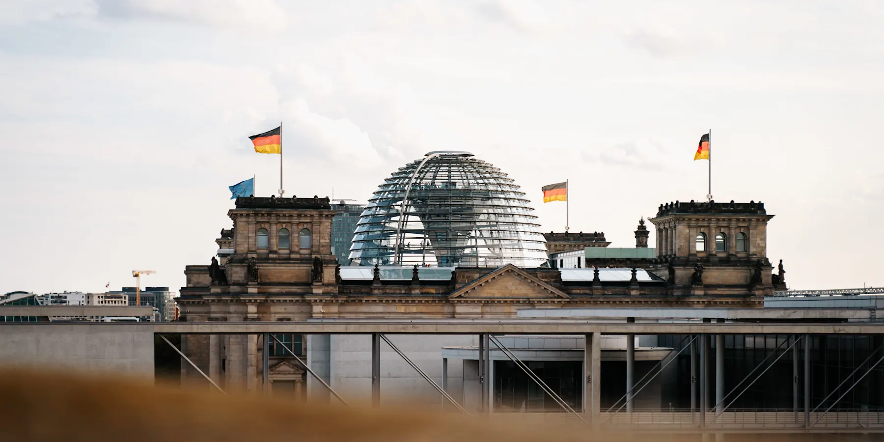 Steinernes Gebäude mit Glaskuppel und mehreren deutschen Flaggen auf dem Dach.