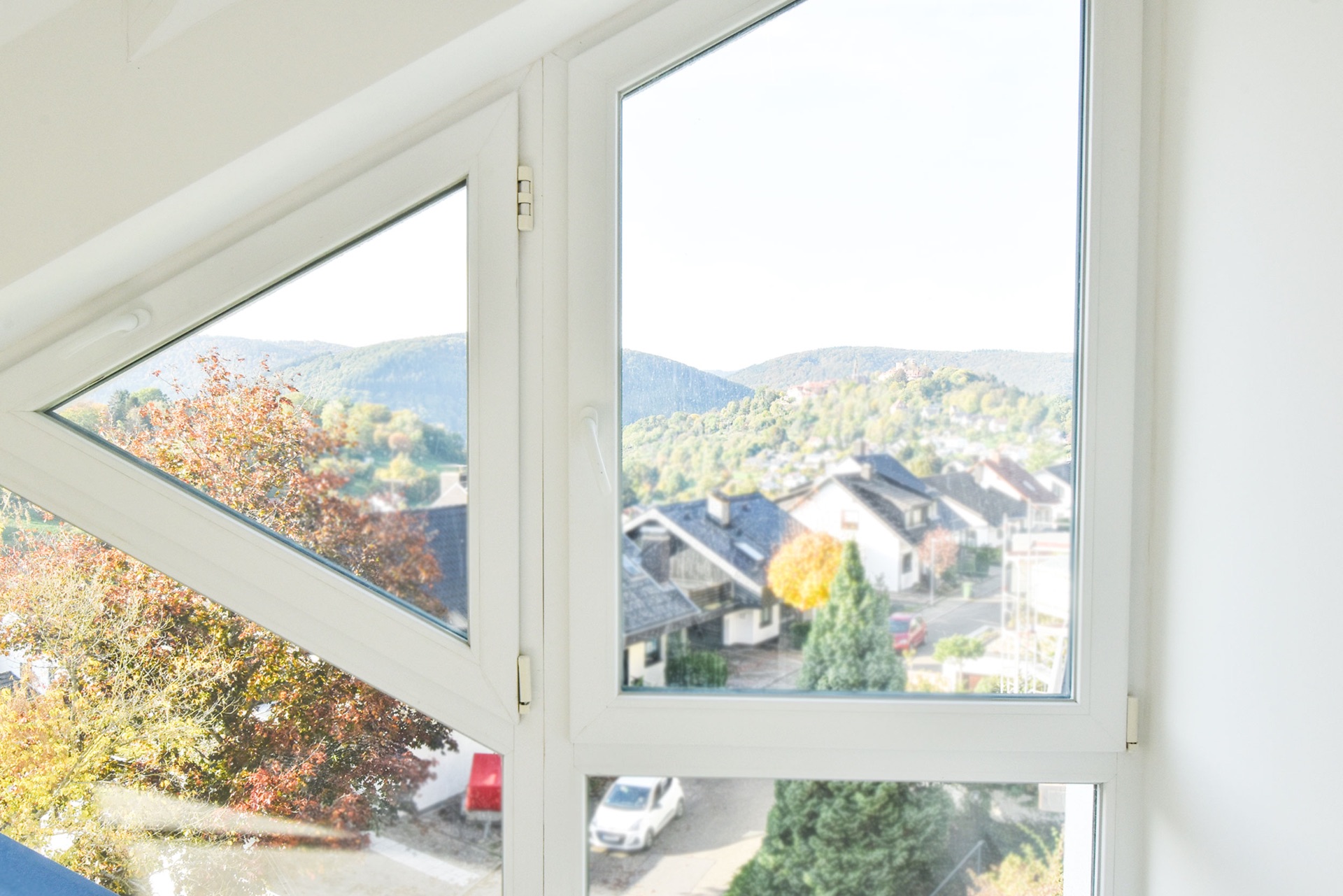 Blick durch ein großes Fenster auf Wohnhäuser, Bäume und Hügel im Hintergrund.