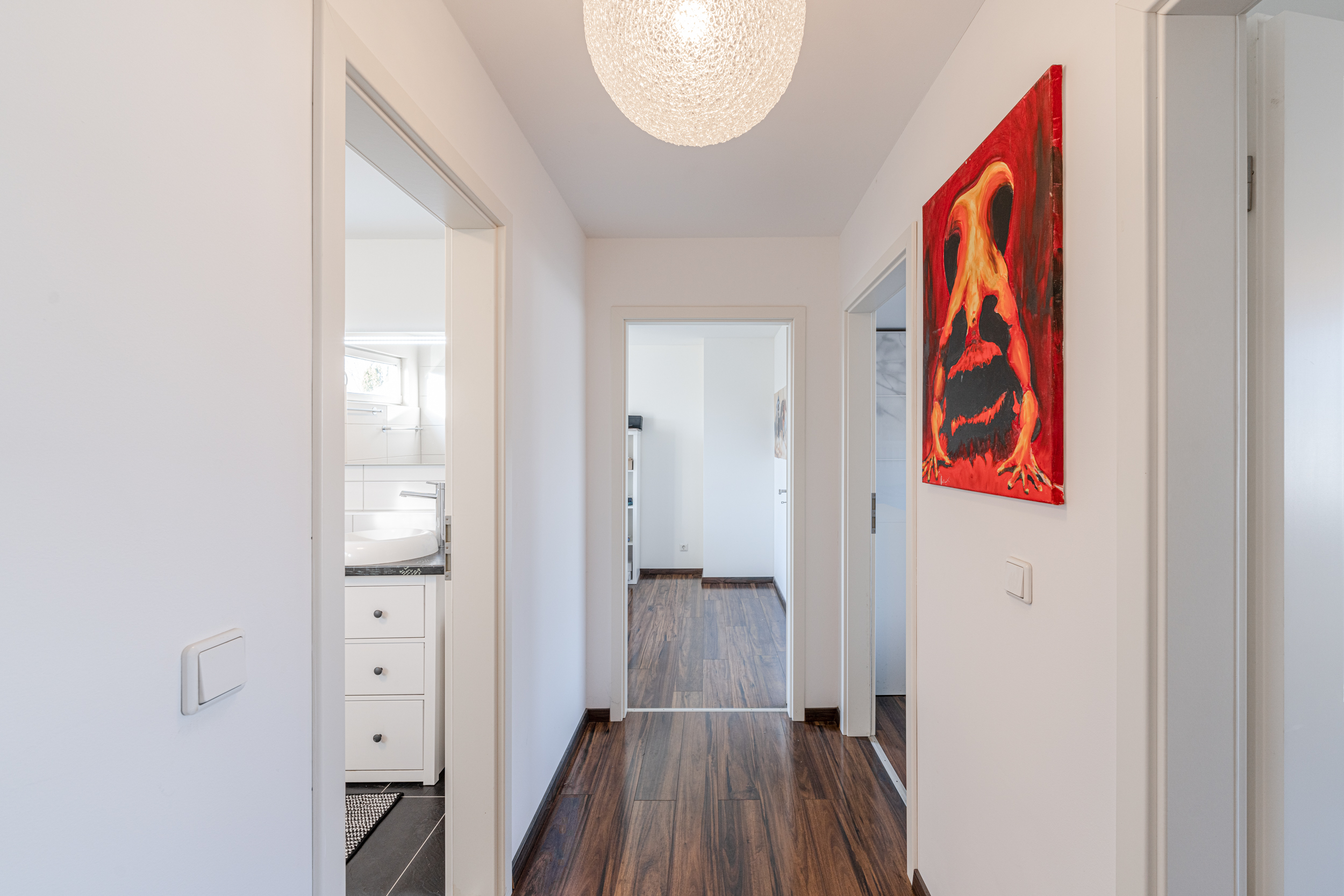 Heller Flur mit Holzboden, weißen Türen und abstraktem roten Gemälde an der Wand.