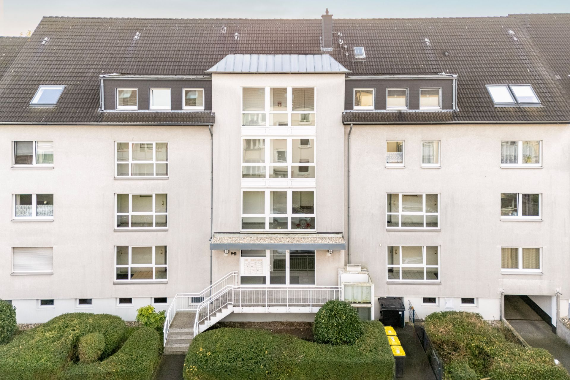 Mehrfamilienhaus mit mehreren Fenstern, Eingangsbereich, Rampe und Vorgarten.